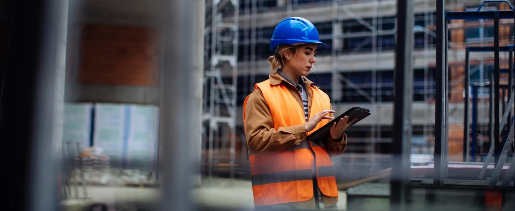 Une femme équipée d'EPI est sur un chantier avec une tablette dans les mains