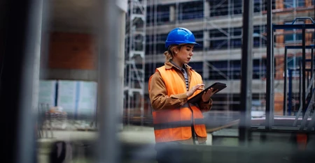 Une femme équipée d'EPI est sur un chantier avec une tablette dans les mains